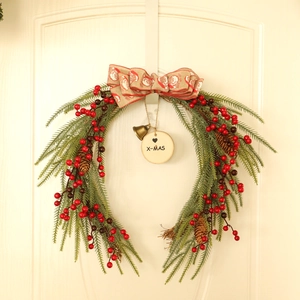 Christmas wreath with green pine branches, red berries and X-MAS wooden sign on white door