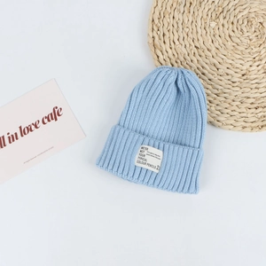 Detailed view of light blue ribbed knit beanie with white textile label on white surface