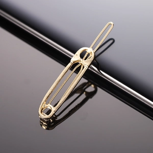 Minimalist gold safety pin hair clip with high-shine metallic finish on reflective surface