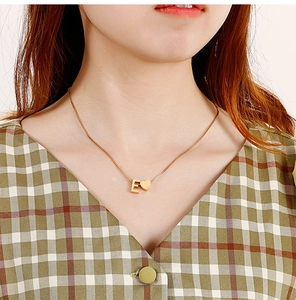 Detail of gold titanium necklace featuring a capital letter E and a small heart charm