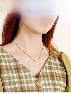 Close-up of a gold heart pendant with letter L on a sleek chain worn by a model