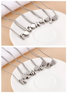Close-up of heart-shaped letter necklaces F to O in a white ceramic dish