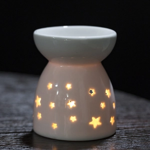 White ceramic aromatherapy lamp with star cutouts glowing warmly on wooden surface