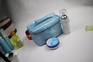 Blue makeup bag with letter prints and top handle shown with various cosmetic bottles