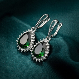 Macro shot of pear-cut emerald earrings with zirconia pavé on green silk background