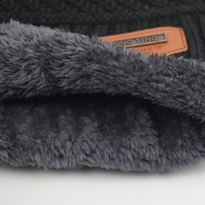 Detail of warm black knit beanie featuring thick grey faux fur lining and leather logo patch