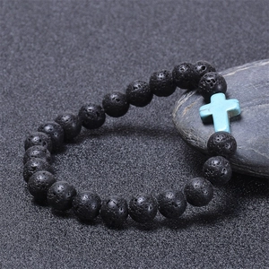 Detailed view of black lava rock beads and a blue turquoise cross on a textured stone