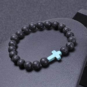 Macro detail of black lava stone beads with a blue turquoise cross on a textured display