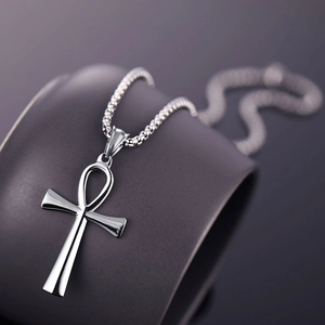 Close-up of silver Ankh cross pendant with bead chain draped on ceramic vessel