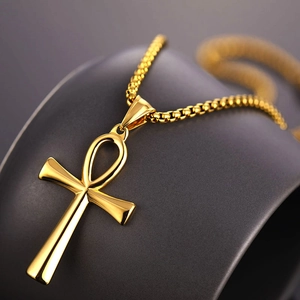 Detail of golden Ankh cross pendant on a thin box chain over a soft grey surface