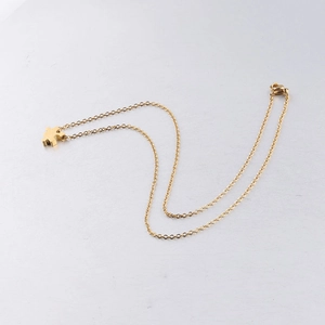 Polished gold puzzle piece pendant necklace with fine cable chain on a textured surface