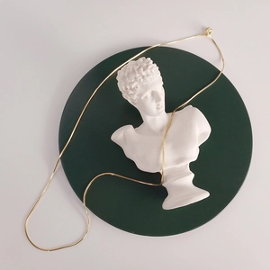 Artistic display of a gold snake bone chain necklace on a white bust statue