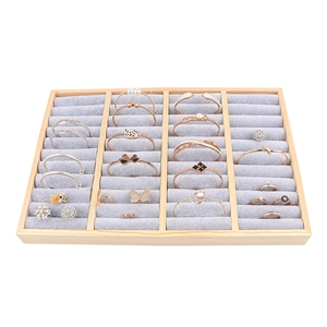 Wooden jewelry tray with grey velvet compartments showcasing rings and bracelets