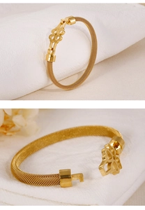 Macro view of gold woven mesh bracelet featuring a hollow four-leaf clover clasp
