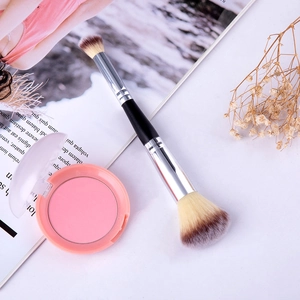 Gros plan d'un pinceau de maquillage double embout et d'un fard à joues rose sur un bureau