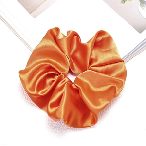 Detailed view of glossy orange satin scrunchie with silky texture for hair styling