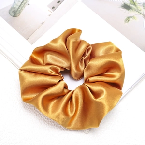 Detail eines goldenen Satin-Haargummis mit glatter Seidentextur und eleganten Falten