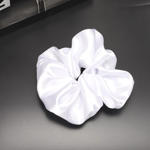 Detail showing the glossy texture and folds of a white satin silk scrunchie on dark background