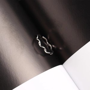 Close-up of a minimalist silver twisted wave ring placed in a dark paper crease