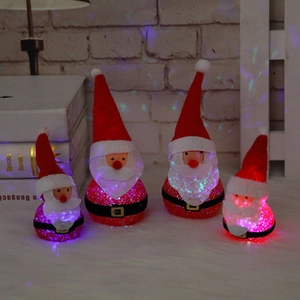 Detail of four light-up Santa Claus figurines with LED glowing beards and red velvet hats