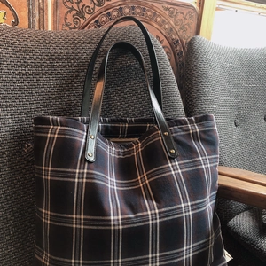 Detail of checkered tote bag featuring navy blue grid and black leather handles with rivets