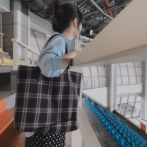 Large plaid tote bag with black leather straps worn over the shoulder in a stadium