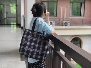 Close-up of black and white plaid tote bag featuring leather handles and metal rivets