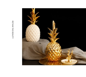 Detail of ceramic pineapple decor and golden deer jewelry tray on a grey fabric base