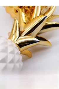 Macro detail of electroplated golden leaves and white ceramic pineapple sculpture