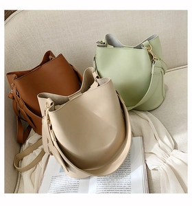 Minimalist bucket bags in brown, green and beige displayed on a soft sofa