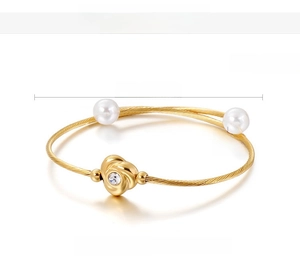 Détail d'un bracelet jonc en acier doré avec perles de coquillage et motif rose