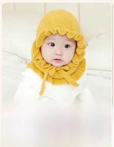 Detail of yellow knit baby winter hat with ruffled edges and chin straps for warmth