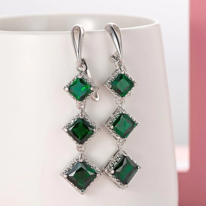 Macro detail of silver drop earrings featuring three deep green square-cut gemstones