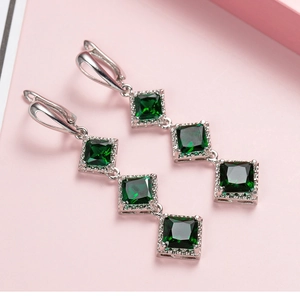 Macro shot of long drop earrings featuring emerald green square stones in silver settings