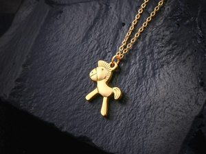 Vue macro du pendentif petit cheval en or 18 carats sur fond de pierre texturée sombre