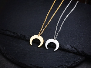 Detailed view of 18K gold and silver crescent moon pendant necklaces on stone background