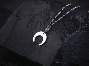 Macro shot of silver crescent moon pendant on fine chain over a dark textured rock