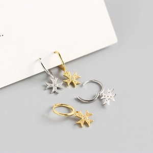 Detailed macro view of silver and gold huggie hoop earrings with sparkling star pendants