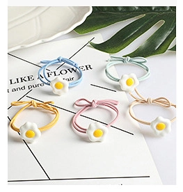 Detail view of five pastel scrunchies with white flower charms on a decorative card