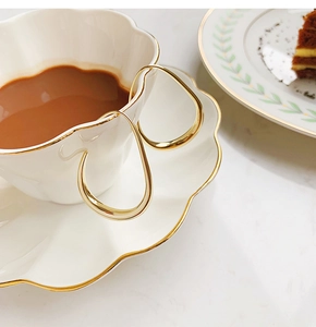 Detailed view of irregular gold hoop earrings resting on a white ceramic coffee cup rim