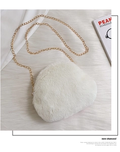 Detail of white plush shoulder bag with golden chain strap on a soft fur background