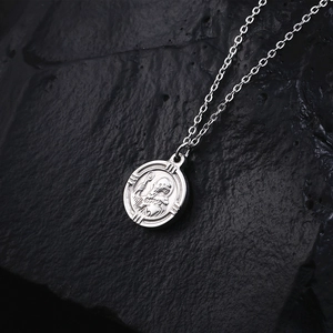 Collier avec pendentif pièce de monnaie en relief argenté sur un fond en pierre sombre