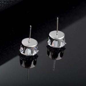 Macro shot of silver stud earrings with clear round-cut zircon on a black reflective surface