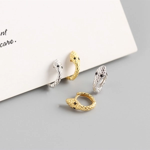 Macro shot of gold and silver snake earrings with black stone eyes and polished finish