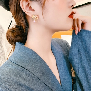 Elegant gold fireworks stud earrings with zircon crystals worn by a model in soft light