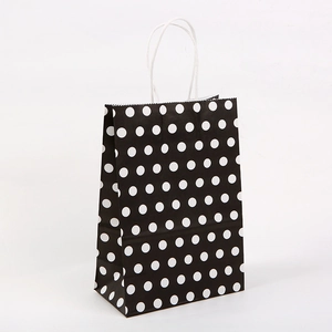 Détail d'un sac cadeau en papier kraft à pois noirs et blancs avec poignées blanches