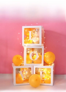 Close-up of four transparent LOVE letter boxes with orange balloons and LED string lights