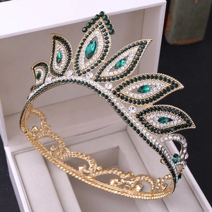 Macro detail of ornate gold bridal crown featuring green and clear crystals in white gift box