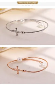 Detail of twisted cable bangles with metal cross and white pearls in silver and rose gold