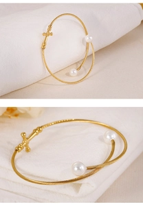 Macro detail of gold-plated twisted cable bracelet featuring white pearls and a cross charm